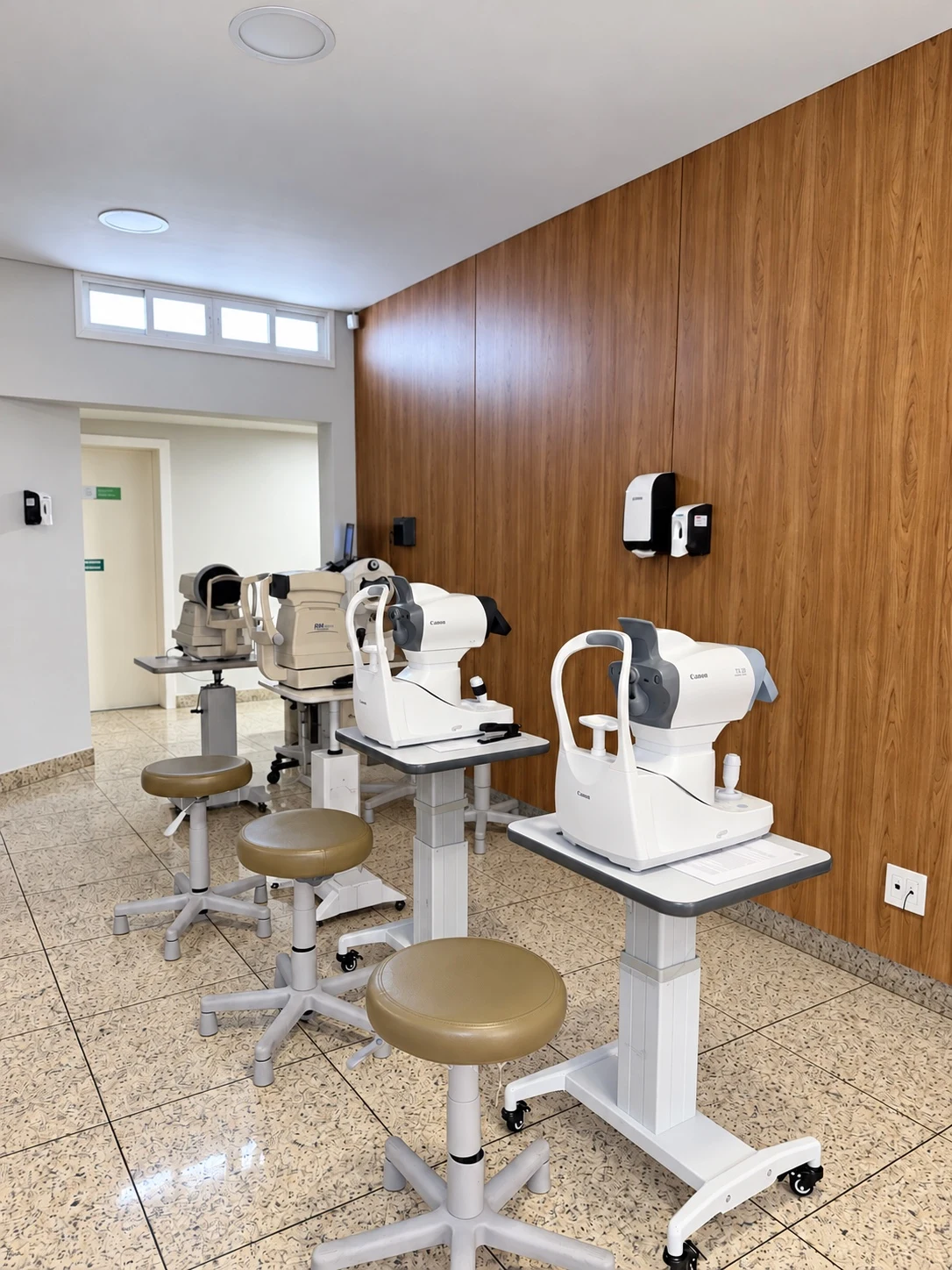 Sala de exames do IOSG com aparelhos oftalmológicos alinhados junto à parede de madeira e banquetas de atendimento.